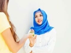 Caucasian girl stretching an apple to muslim woman